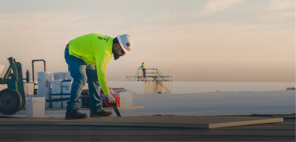 King of Texas crew installing roofing materials on a large commercial flat roof at sunrise.