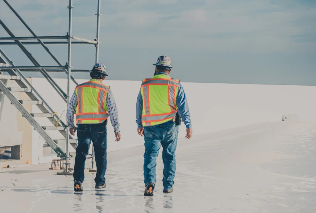 Commercial roofing supervisors walking across white flat roof during project inspection.